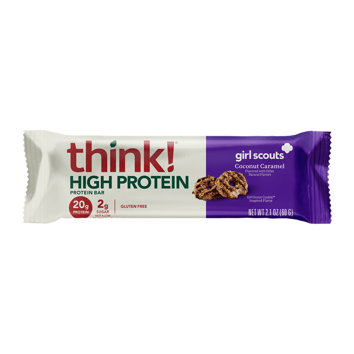 Protein bar wrapper with "think! High Protein" in red and green. It features the Girl Scouts logo and image of coconut caramel cookies, conveying a sweet, healthy snack.