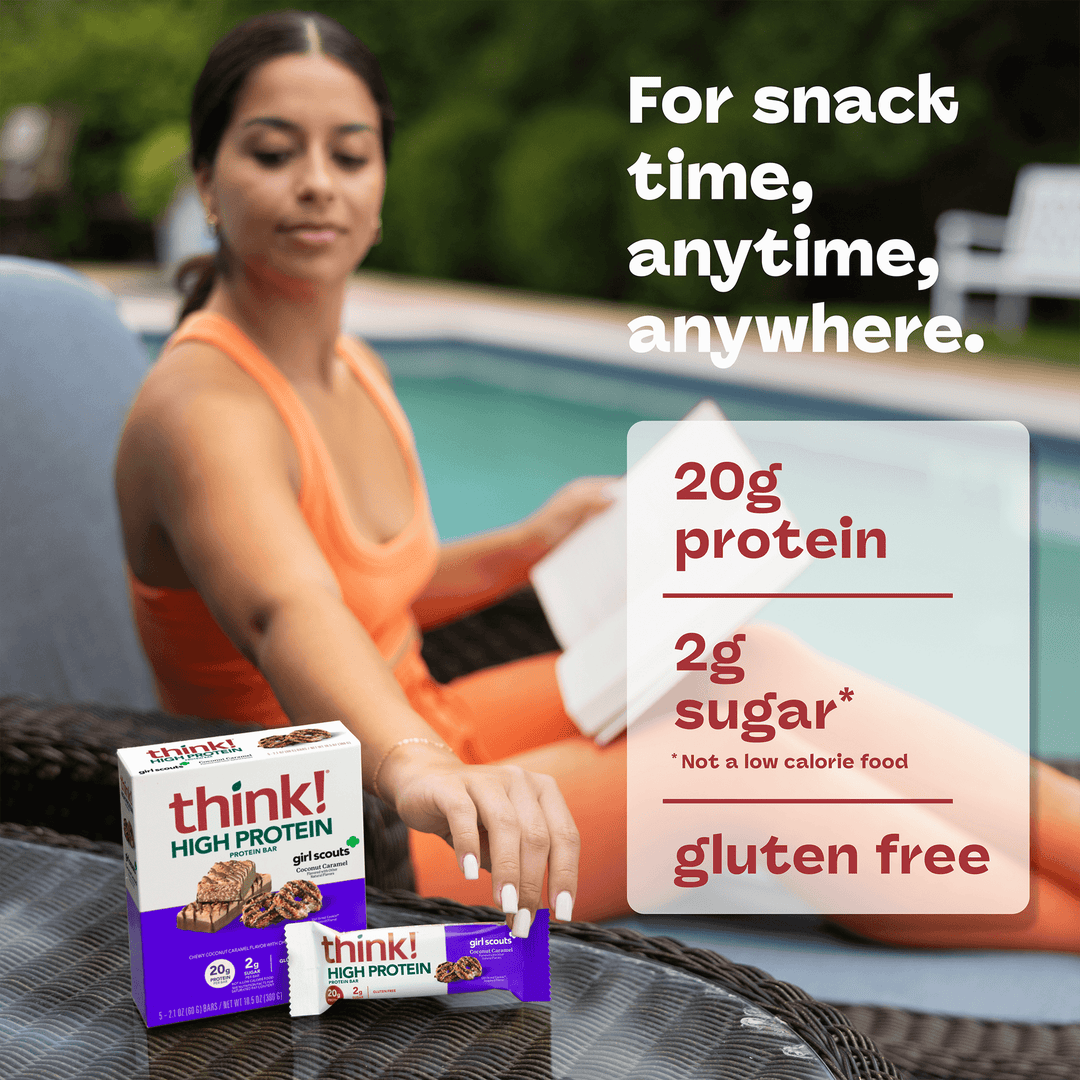A woman in an orange outfit relaxes by a pool, holding an open book. In front of her is a box and bar of "think! High Protein" snacks. Text reads, "For snack time, anytime, anywhere," highlighting 20g protein, 2g sugar, and gluten-free.