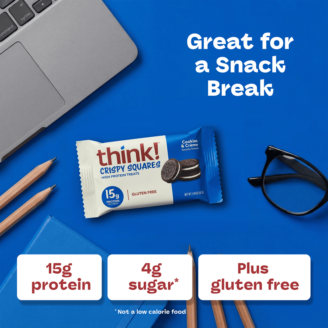 Snack bar with "think! Crispy Squares" packaging on a blue desk with pencils, glasses, and a laptop. Text highlights 15g protein, 4g sugar, gluten-free.